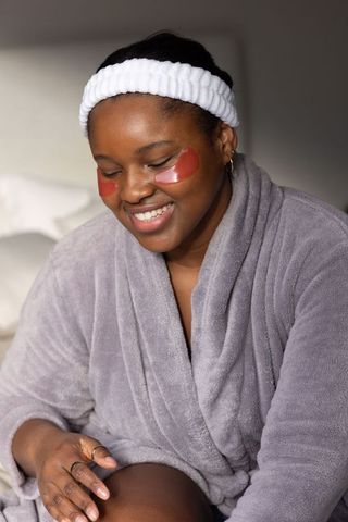 African american woman smiling with under-eye gel patches wearing gray robe and headband