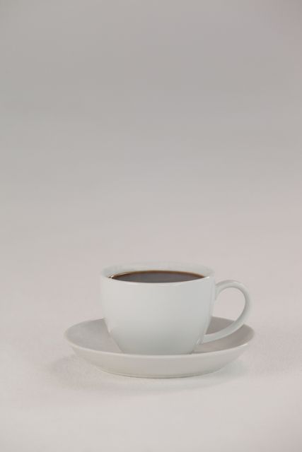 Cup of black coffee on saucer against white background