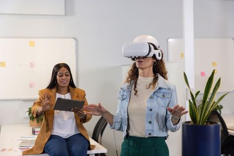 Diverse female coworkers testing VR headset during modern office collaboration