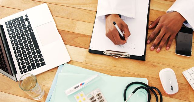 Doctor Writing Notes In Clipboard On Wooden Desk With Laptop And Medical Supplies - Download Free Stock Images Pikwizard.com