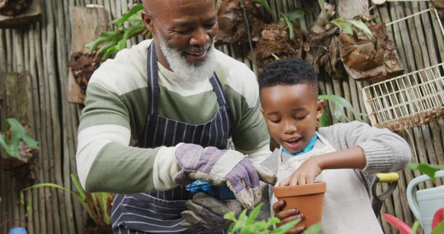 Grandfather guides young boy while they pot a plant in outdoor garden. Both smiling and enjoying the activity. Represents family values, bonding time, and teaching moments. Perfect for use in articles and advertisements about family activities, gardening hobbies, and educational moments.