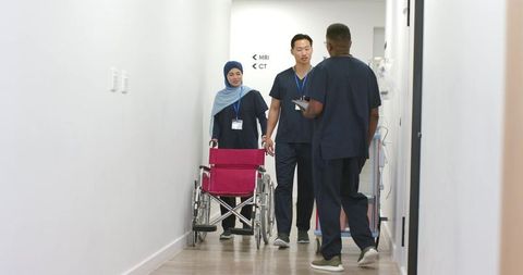 Diverse medical team walking hospital corridor pushing wheelchair toward mri ct