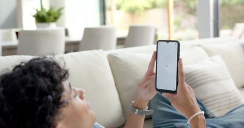 Man reclining on sofa holding smartphone with blank screen in sunlit modern living room
