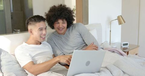 Diverse Male Friends Relaxing in Bedroom and Using Laptop