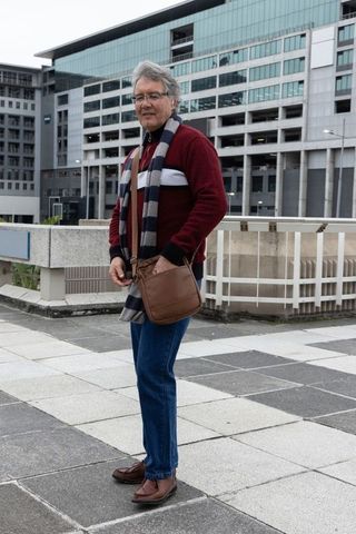 Senior man standing on urban terrace wearing red sweater carrying brown leather bag