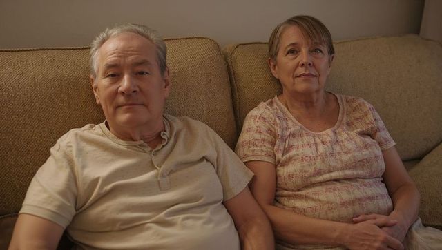 Senior couple sitting together on couch looking thoughtful cozy home interior evening light