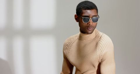 Stylish man wearing turtleneck sweater and sunglasses in modern interior