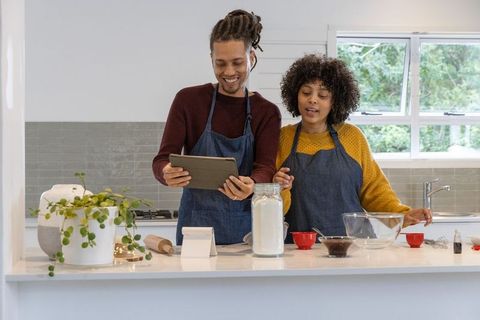 Couple following recipe on tablet and baking together in bright modern kitchen