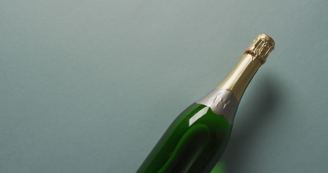 Green champagne bottle with gold foil on cork lying on blue background. Ideal for illustrating festive celebrations, luxury events, parties, and beverage advertisements. Suitable for banners, posters, social media graphics, or invitation designs.
