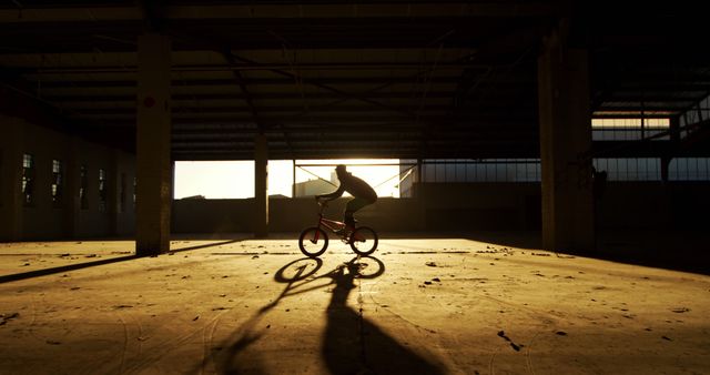 Silhouette of BMX biker riding in deserted warehouse at sunset - Download Free Stock Images Pikwizard.com