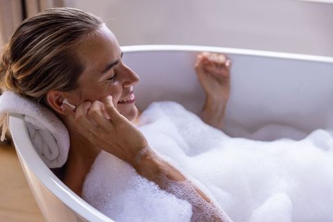 Woman relaxing in bubble bath listening to earbuds, enjoying self-care and wellness