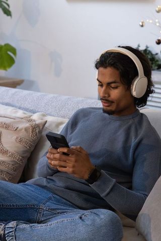 Young man reclining on sofa wearing headphones and smartwatch, using smartphone, relaxing