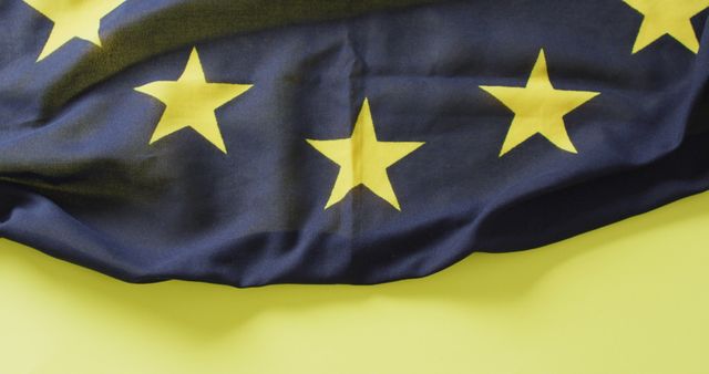 Image shows a close-up view of the European Union flag with its yellow stars on a blue background, alongside a bright yellow surface. Suitable for illustrating topics related to the European Union, international relations, patriotism, and unity. Great for websites, articles, or presentations concerning European politics, cultural events, and EU symbols.