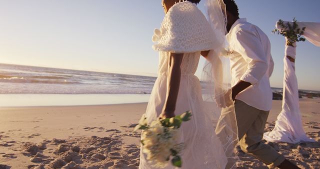 African american couple in love getting married, holding hands on the beach at sunset. marriage, love and romance, holiday by the sea.
