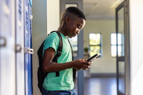 African american teen leaning by lockers texting on smartphone in school hallway