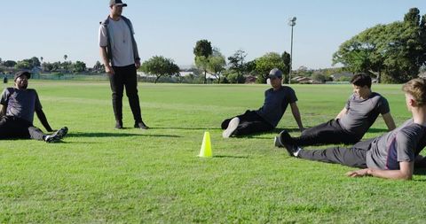 Coach instructing baseball players on green field with yellow cone running teamwork drills