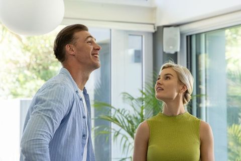 Couple looking up in bright modern living room with glass doors and indoor greenery