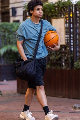 Young african american man walking with basketball and duffel bag in urban street