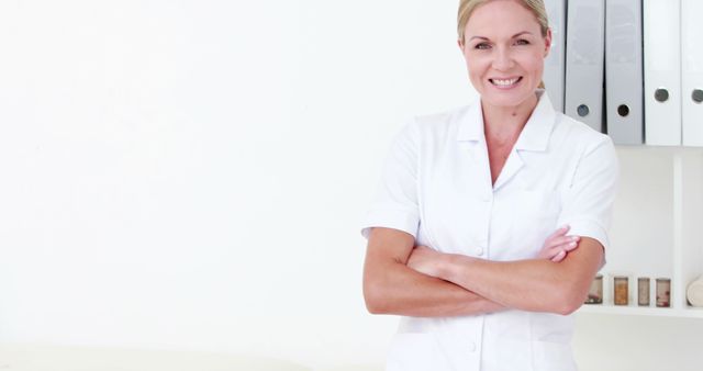 Female healthcare professional standing in a medical office, smiling confidently with arms crossed. Suitable for healthcare advertisements, medical websites, professional healthcare publications, and educational medical materials highlighting medical professionals' reliability and approachability.