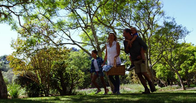 Family strolling through lush park holding picnic basket. Great for themes of family bonding, leisure activities, outdoor enjoyment, and healthy lifestyle. Can be used in advertisements for picnic products, family gatherings, parks, and recreational areas.