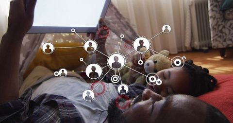 Father and daughter lying together using tablet with network overlay bedtime bonding