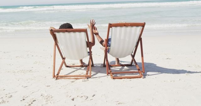 African american couple holding hands and lying on sunbeds on sunny beach - Download Free Stock Photos Pikwizard.com