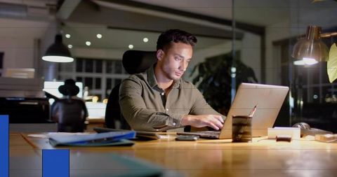 Focused professional working late on laptop in modern office with warm desk lamp