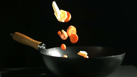 Chopped Vegetables Falling into Wok in Slow Motion on Black Background