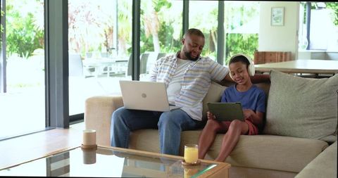 African american father working on laptop while son learning on tablet at home