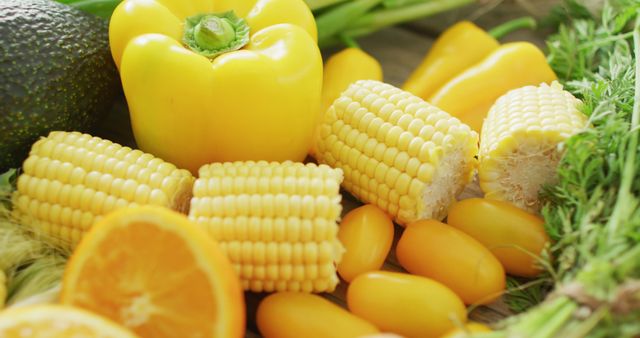 Yellow bell peppers, corn cobs, tomatoes, avocado, orange slices, and leafy greens arranged on table. Perfect for use in healthy eating and lifestyle promotions, food blogs, culinary arts, dietary guides, and organic agriculture campaigns.