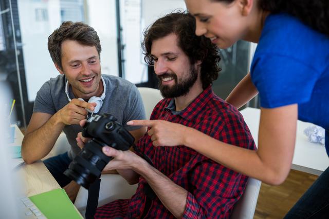 Creative professionals reviewing photos on a camera in a modern office. Ideal for use in articles or advertisements about teamwork, creative industries, modern work environments, and professional collaboration.
