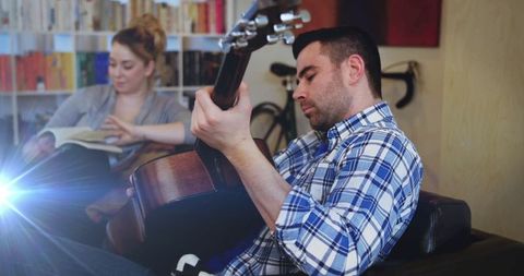 Man Playing Acoustic Guitar While Woman Reads in Cozy Living Room