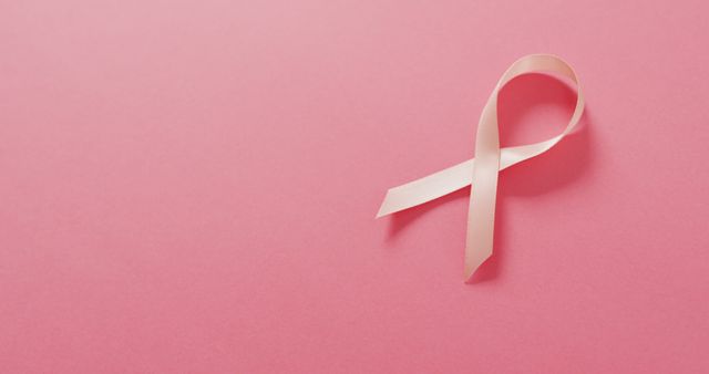 Pink ribbon lying on pink background signifying breast cancer awareness. Suitable for use in breast cancer awareness campaigns, charity events, healthcare promotions, social media posts, and informational brochures.