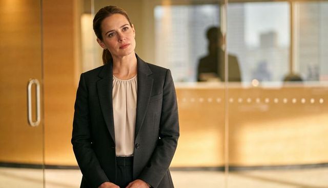 Thoughtful executive businesswoman standing in modern glass office lobby wearing dark suit
