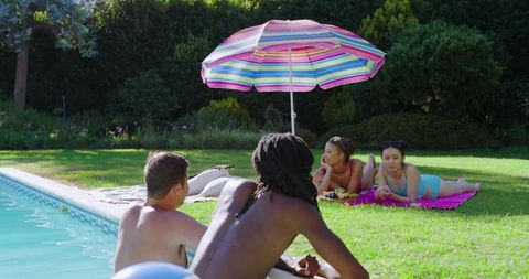 Diverse friends relaxing by pool with colorful umbrella