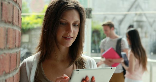 Young Woman Using Tablet Outdoors with Friends in Background - Download Free Stock Images Pikwizard.com