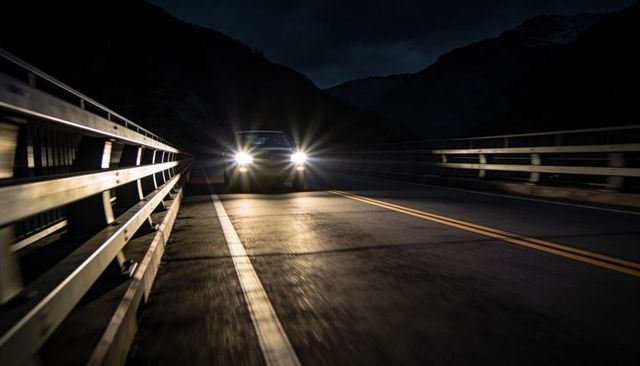 Driving car crossing bridge at night with bright headlights and reflective guardrails