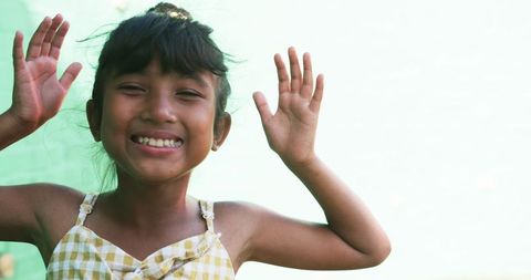 Cheerful Young Girl in Yellow Dress Raising Hands Happily