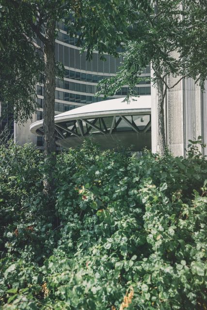 This image depicts a modern architectural building with a circular roof design partially hidden by lush greenery. It shows the harmony between urban development and nature. Perfect for themes related to urban planning, sustainability, architectural design, and green living.