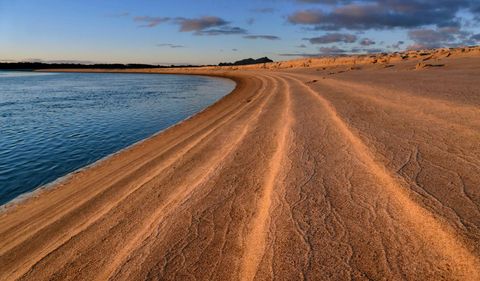 Curving sand ridges guiding eye along golden shoreline of calm coastal lagoon