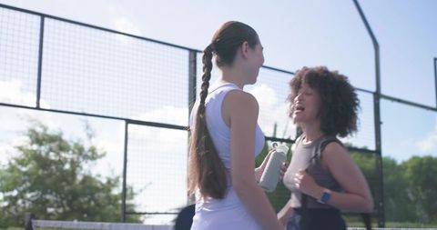 Diverse female friends chatting on outdoor padel court during sunny training break