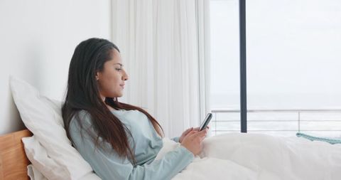 Relaxed Woman Enjoys Leisurely Morning with Smartphone in Minimalist Bedroom