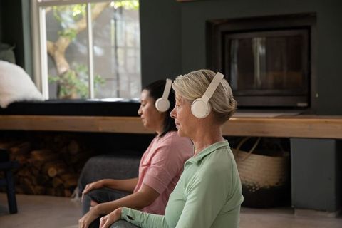 Mature women meditating with over-ear headphones, practicing mindfulness in cozy home wellness space