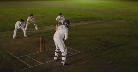 Night cricket action: batsman preparing shot with close-in fielders under floodlights