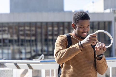 African american man unpacking wireless headphones on sunlit urban terrace with backpack