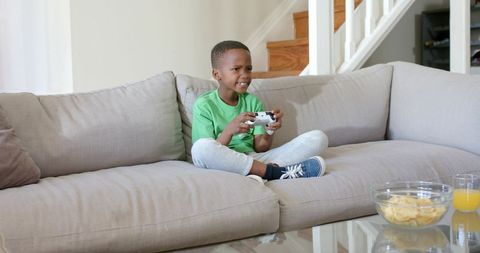 Young African American Boy Playing Video Games on Couch Holding White Game Controller