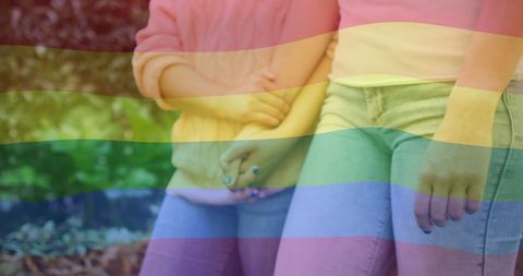 Diverse Female Couple Holding Hands Under Rainbow
