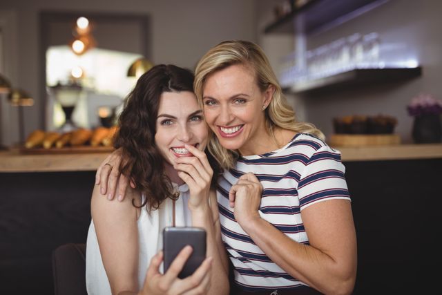 Portrait of happy friends using mobile phone in restaurant