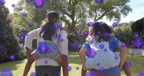 Parents carrying children on shoulders walking sunlit backyard, purple tech icons overlay