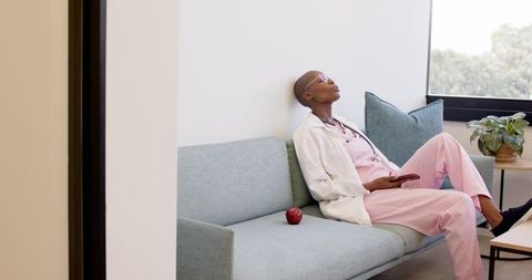Nurse resting on lounge couch during break in clinic wearing pink scrubs with stethoscope